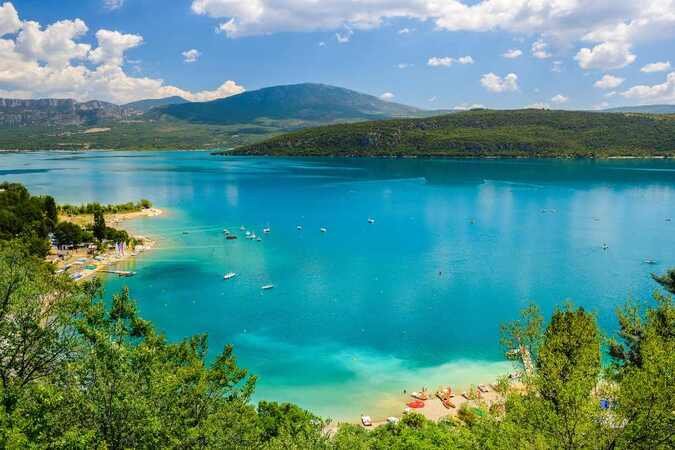 Vue panoramique du Lac de Sainte-Croix avec plages, bateaux et collines verdoyantes sous un ciel bleu d’été